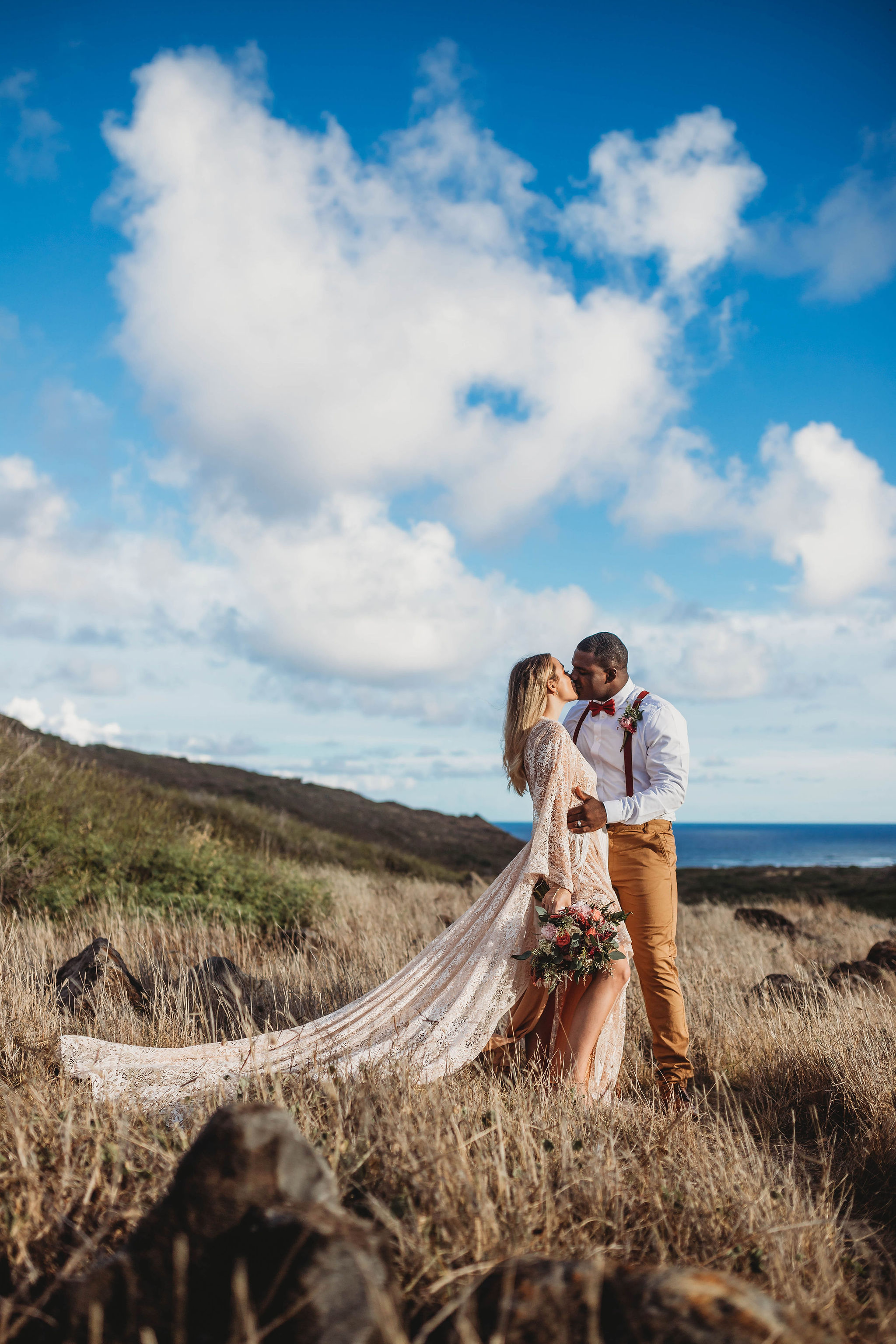 Wedding and Photographer, bride and groom kiss on a dry grassy hill near the ocean