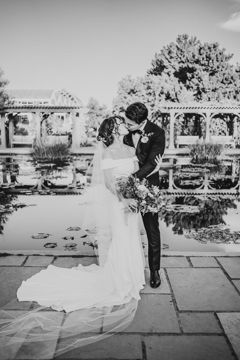 Wedding and Photographer, bride and groom kiss before a reflecting pond and promenade
