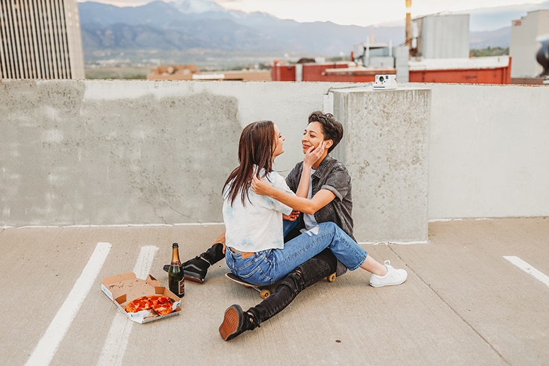 Wedding and Photographer, two partners sit facing each other on a rooftop parking lot, pizza and beer beside them