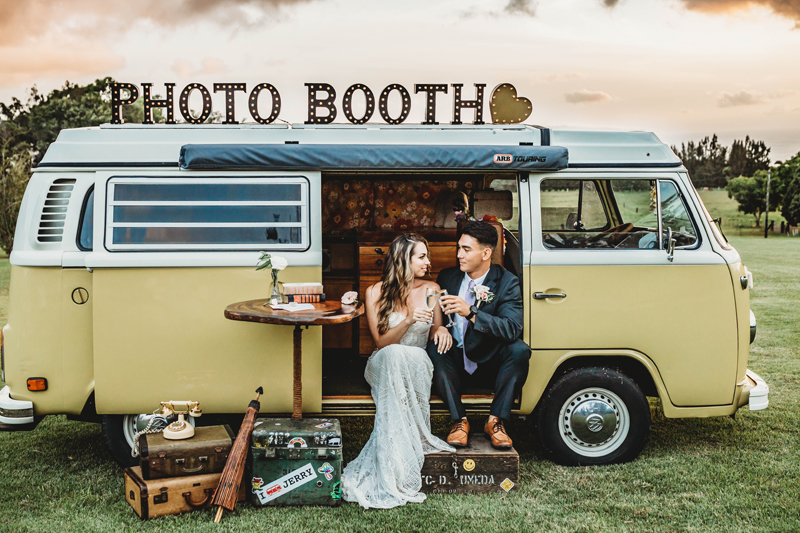 Wedding & Elopement Photographer, bride and groom sit in a decorated Volkswagen bus that reads photo booth atop of it, they toast to champagne