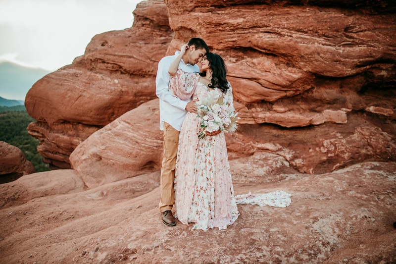 Wedding and Photographer, bride and groom embrace, she wears a floral dress and holds a bouquet