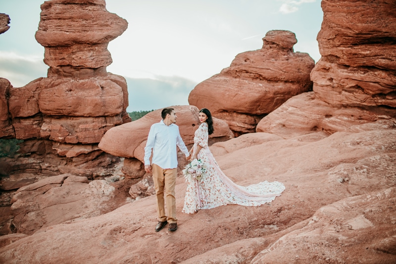 Wedding and Elopement Photography, man and woman hike in desert landscape, she wears floral dress and holds bouquet